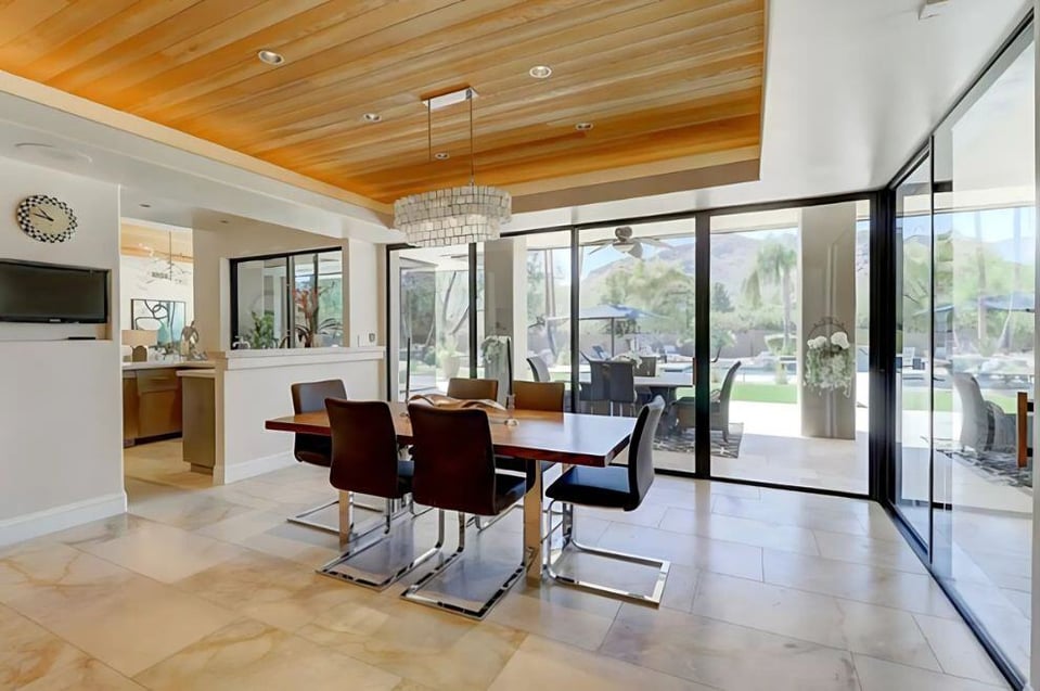 A modern dining area with large glass sliding doors, a natural wood ceiling, and a sleek chandelier.