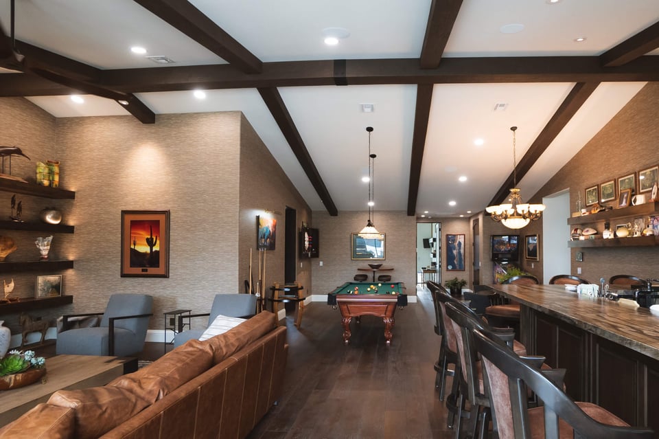 A spacious entertainment room with a modern, rustic design featuring exposed dark wooden beams on the ceiling.