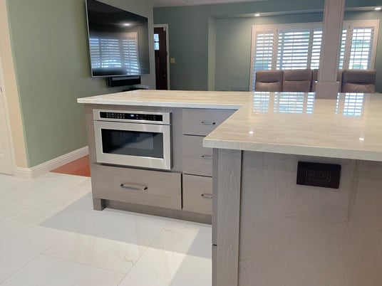 Kitchen island featuring light countertops, built-in microwave, and ample storage.