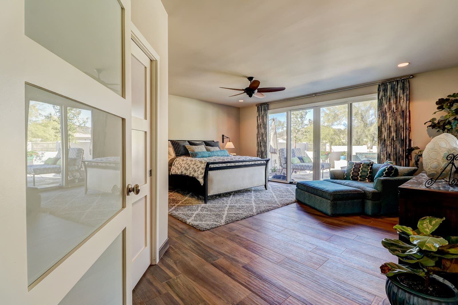 Master bedroom with a glass door leading to a patio, featuring a chaise lounge and wooden floors in a Phoenix home by MGD Builders